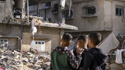 Três homens olham para um prédio danificado destruído por um ataque israelense.